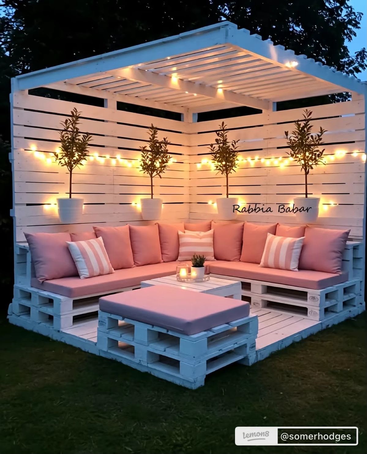 White pallet pergola corner lounge with pink cushions and string lights