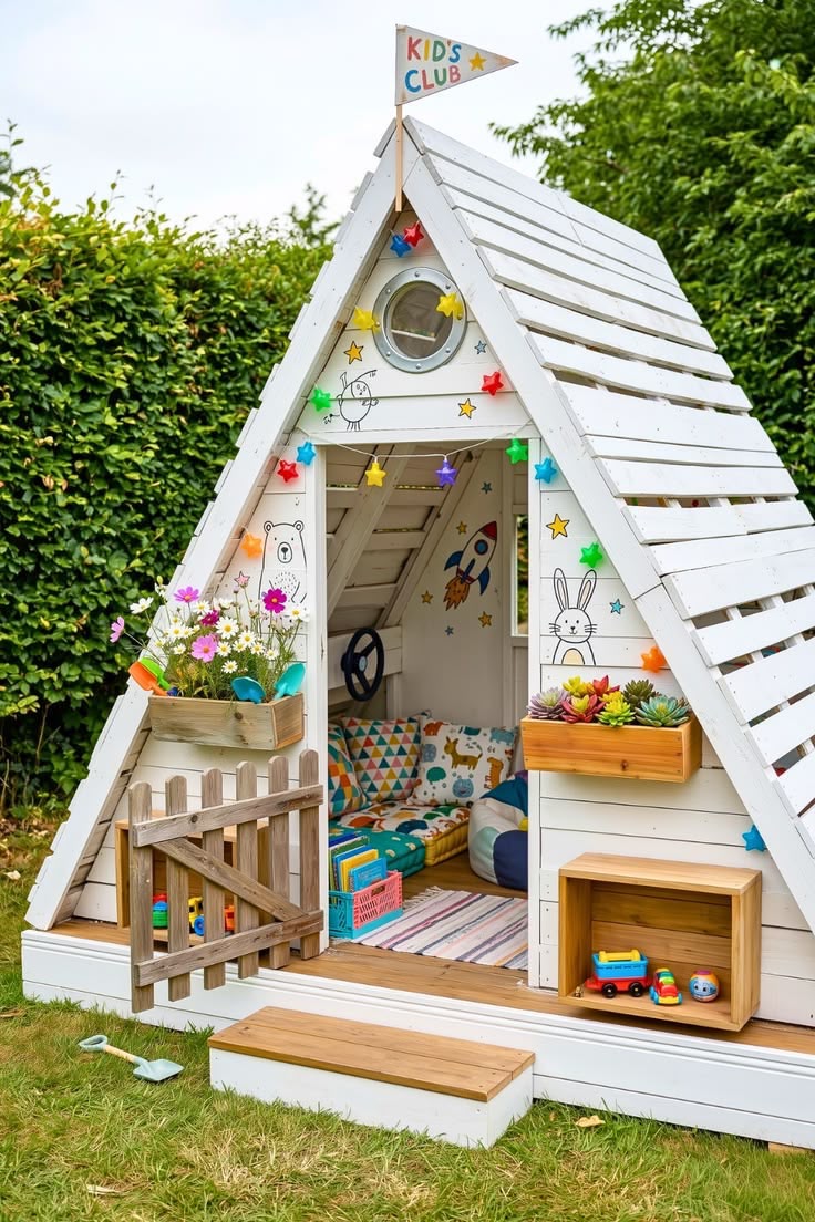 White A-frame pallet kids playhouse with porthole window, picket gate and flag